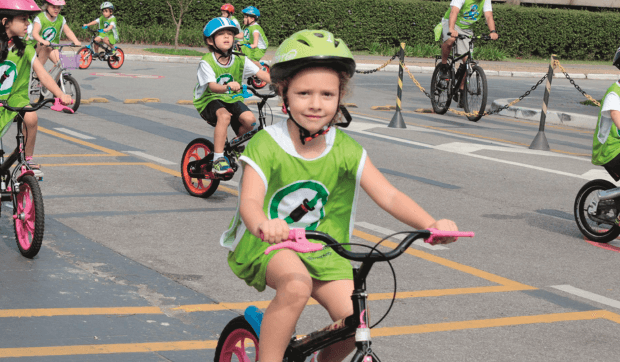 Mehrere Kinder auf Fahrrädern sind mit Helm und Weste auf einem Parkplatz unterwegs